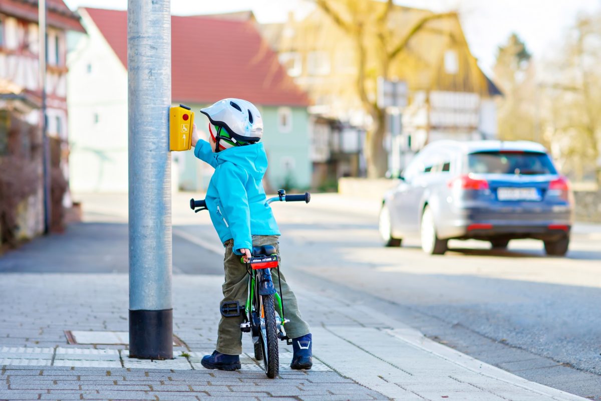 Little preschool kid boy riding with his first green bike in the city. Happy child in colorful clothes standing near traffic lights. Active leisure for kids outdoors.