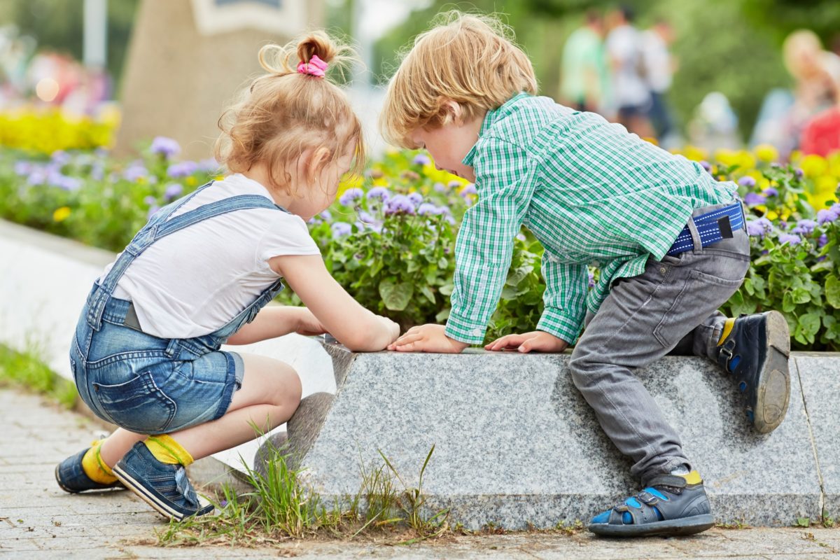 Little boy and girl play at edge of flowerbed on square