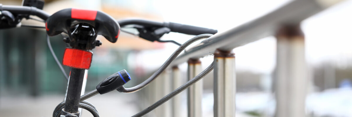 Close-up of red bicycle and protection lock cord on metal handrail. Fixed gear for transport. Street parking outdoors. Safety and vehicle security concept