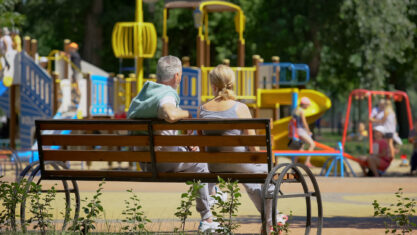 Senior couple sitting on bench near playground, watching grandchildren playing