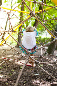 Mädchen spielt im Kletternetz aus Spielplatz. Little child girl climb on play equipment in spider net.