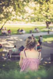 Junges Mädchen sitzt in Gras im Park, Sommer, Aufnahme von hinten