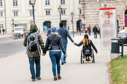 A man with a woman goes by the hand through the streets of Vienna against the background of another couple in love in a wheelchair, disabled love concept