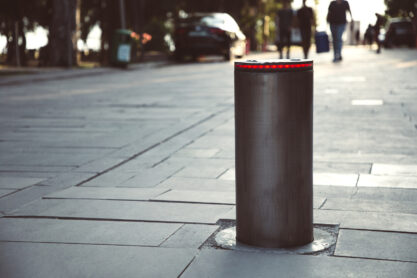 Illuminated retractable automatic traffic bollard protects pedestrian zone. Safety concept. Blurred people on background