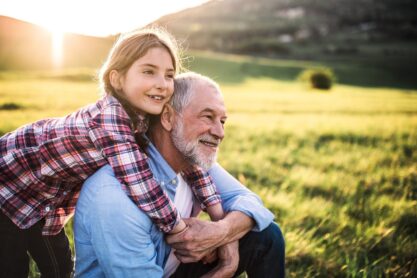 A small girl with grandfather outside in spring nature, relaxing on the grass at sunset.