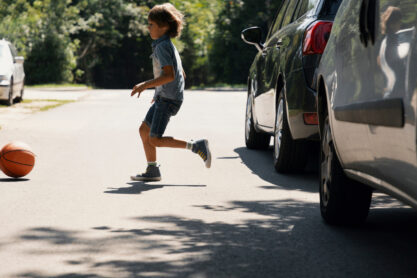 Careless boy running behind the ball on the road next to cars