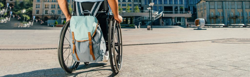 cropped panoramic view of man using wheelchair with bag on street