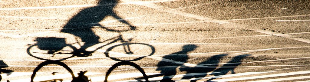 Blurry shadow silhouette of a person riding a bike and pedestrians crossing the street on sunset shiny asphalt with road markings
