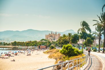 View of the beach of Palma de Mallorca with people lying on sand and the gorgeous cathedral building visible in background. Palma-de-Mallorca, Balearic islands, Spain.