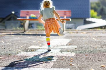 Cute little toddler girl playing hopscotch game drawn with colorful chalks on asphalt. Little active child jumping on playground outdoors on a sunny day. Summer activities for children