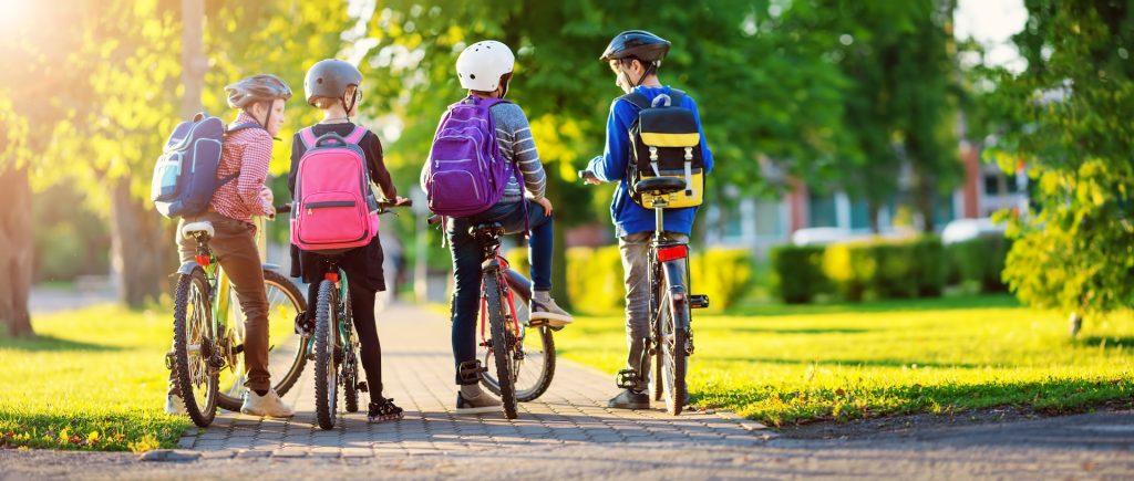 Children with rucksacks riding on bikes in the park near school. Pupils with backpacks outdoors