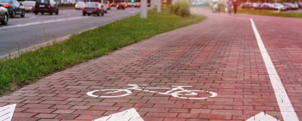 Bike sign painting with white dye on tiled sidewalk near city road with transport traffic. Safety and comfortable facility for biking.