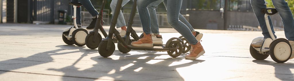 Cropped portrait of a group of millennials having fun while riding electric scooters and segways along the city street. Ecological transportation, friendship concept. Horizontal shot. Side view