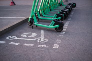 Green electric rent bikes parked in electric scooters parking area, marked with spray paint.