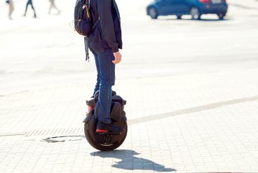 Commuter rides electric monowheel. Man rides an electric unicycle on city street, modern mobility and eco-friendly transportation. View on legs on electric unicycle or mono-wheel on city street