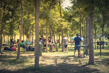 Blurred large group of friend, family members enjoy barbecue on lakeside area. Outdoor camping at natural park with picnic table in Grand Prairie, Texas, USA. Outside Party and BBQ Concept